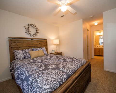A bedroom with a bed, a ceiling fan, and a wreath on the wall.