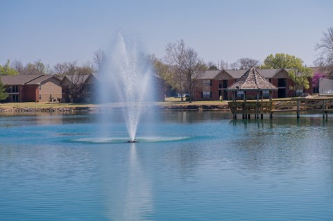 A fountain in the middle of a body of water with houses in the background.