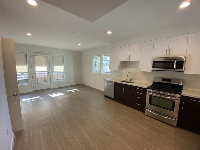 Living room and kitchen area with a sink, dishwasher, gas stove/oven, microwave and cabinets.