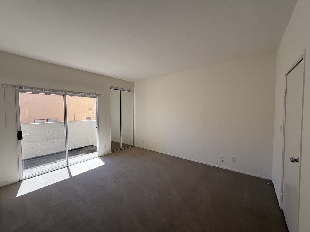 Carpeted bedroom with balcony access a closet.