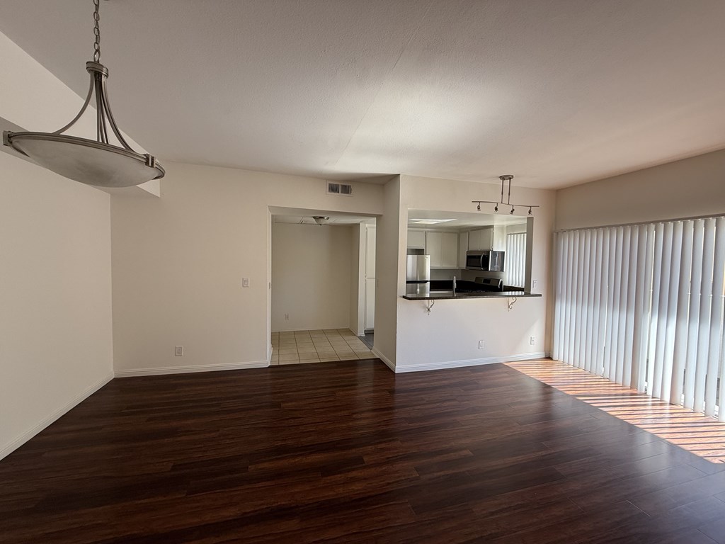 Living room with wood flooring, view of kitchen, a balcony and light fixture.