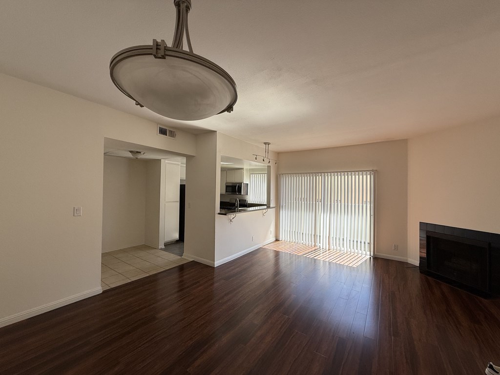Living room with wood flooring kitchen, a fireplace, balcony and light fixture.