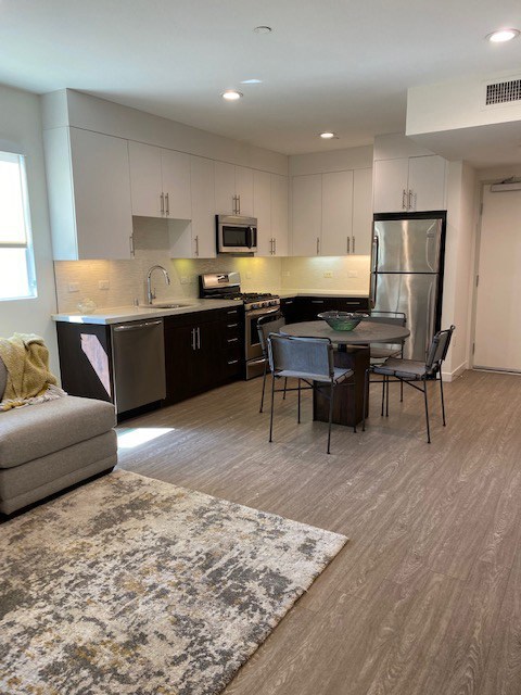 LIving room area and a kitchen with white cabinets, a refrigerator, gas stove, dishwasher and sink.