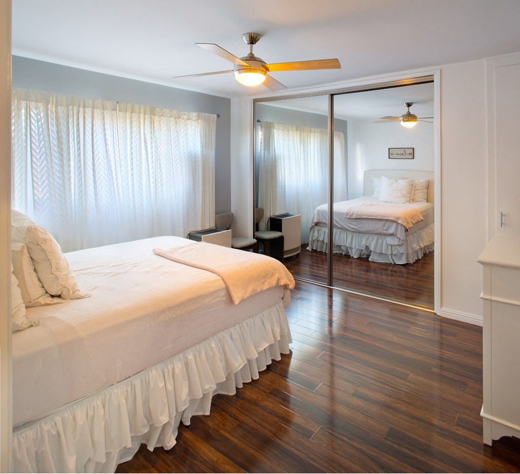 Apartment bedroom with mirrored closet doors, ceiling fan with light