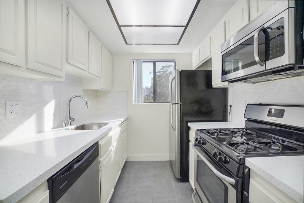 Apartment kitchen with stainless steel appliances, white tile back splash, white counter tops, and white cabinets.