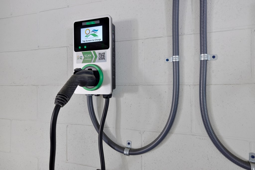 A wall-mounted electric vehicle charging station with a cable plugged in.