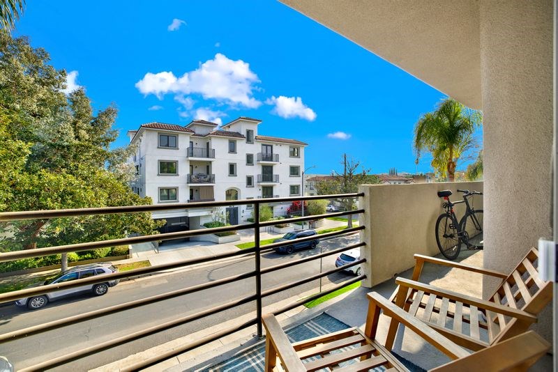 A balcony with a chair and a bicycle is overlooking a street with cars and buildings.