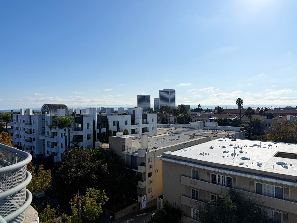 Rooftop cityscape view with buildings and trees under a clear sky.