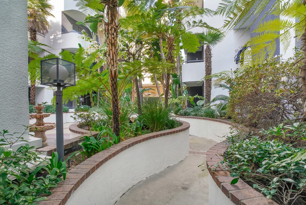 Apartment courtyard with a winding walking path, lush plants and a water feature. at Midvale Court, California, 90024