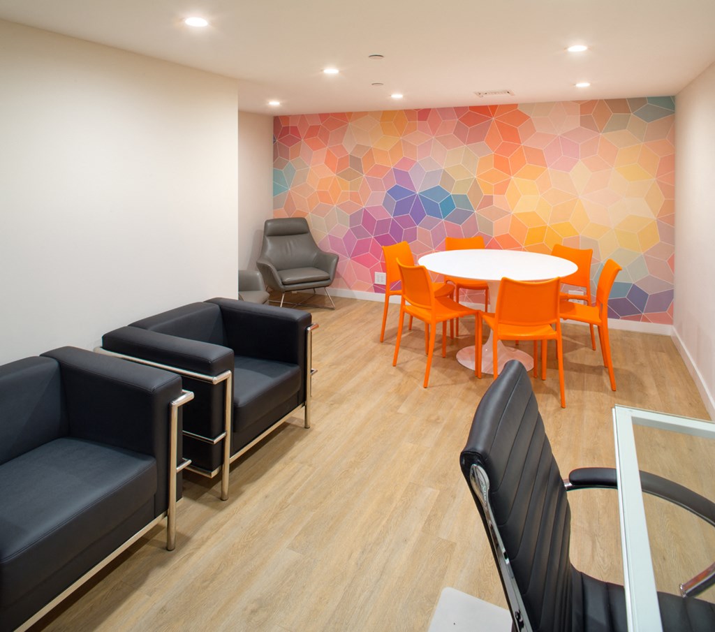Apartment complex lounge with office furniture and a colorful geometric mural. at Midvale Court, Los Angeles