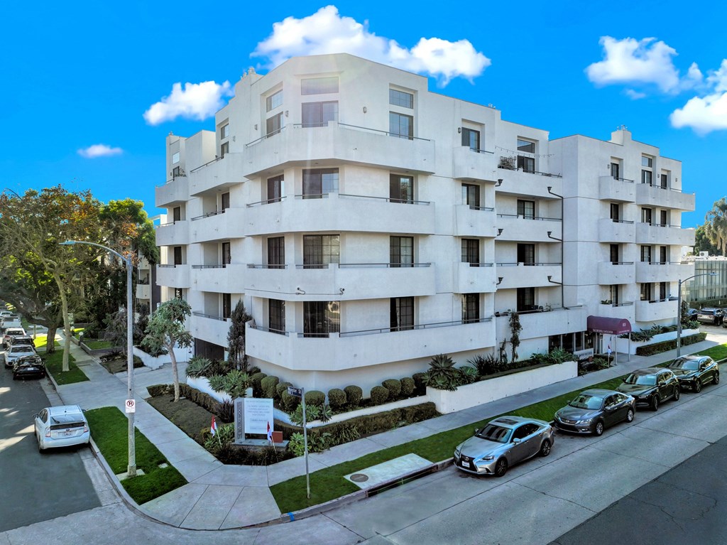 A white apartment building with cars parked in front at Beverly Wooster Apartments, Los Angeles, CA