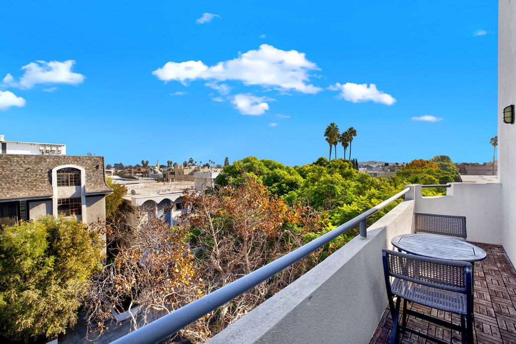 A balcony with a table and chairs overlooks a scenic view of trees and buildings at Beverly Wooster Apartments, Los Angeles, CA 90035