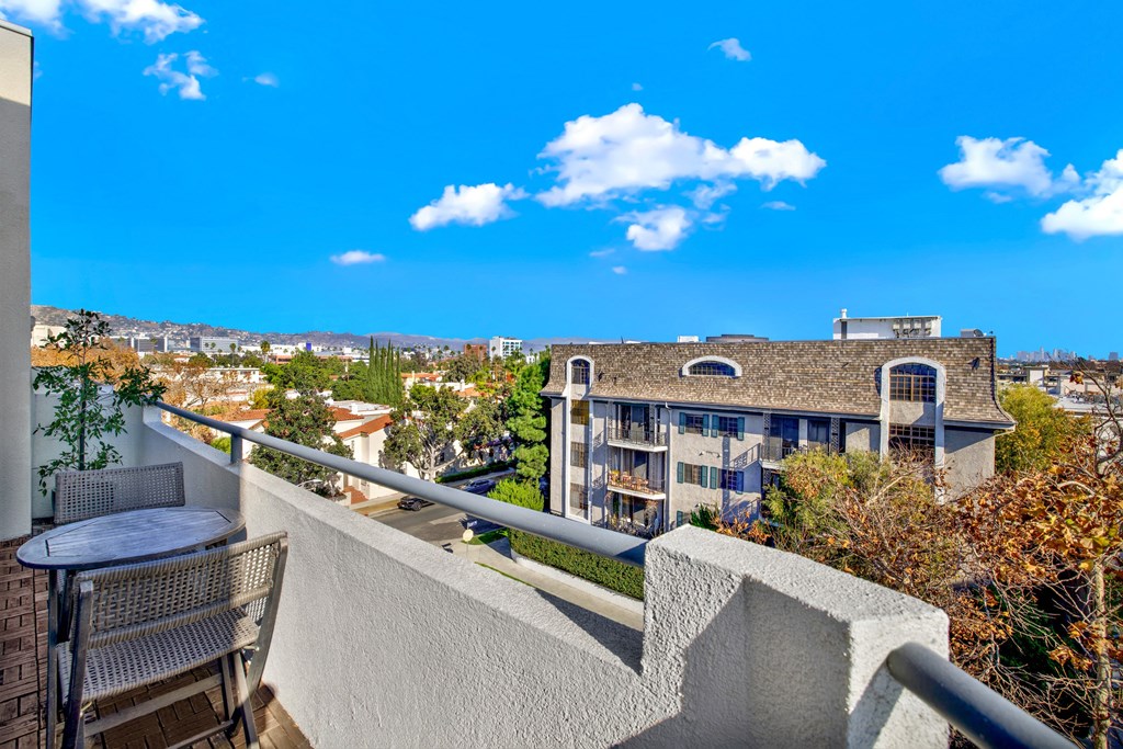 A balcony with a table and chairs overlooks a large building and a green lawn at Beverly Wooster Apartments, California 90035