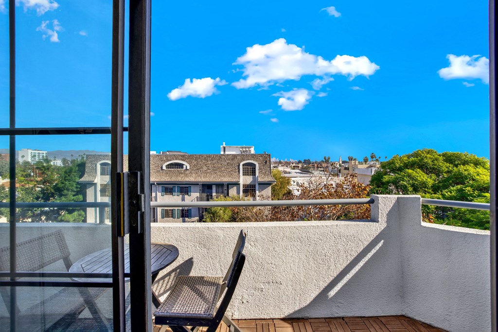 A balcony with a table and chairs overlooks a residential area at Beverly Wooster Apartments, California