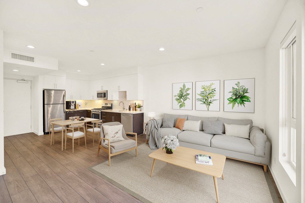 A modern living room with a grey sofa, wooden coffee table, and a kitchen area in the background at The Urbanpolitan, California 90036