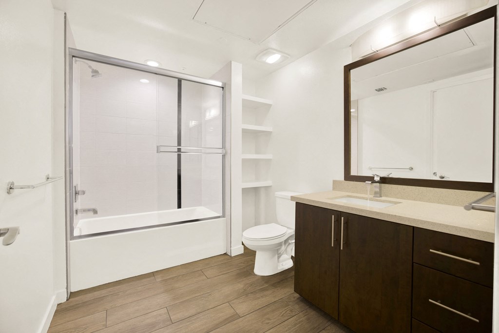 A bathroom with a toilet, sink, and a bathtub with a glass door at The Urbanpolitan, Los Angeles, 90036