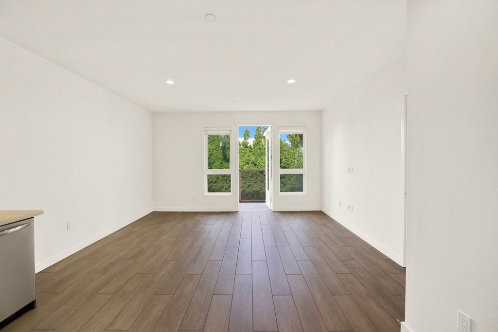A large empty room with a dishwasher on the left and a window with a view of trees outside at The Urbanpolitan, Los Angeles, CA 90036