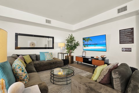 A living room with a grey couch and a TV on the wall.