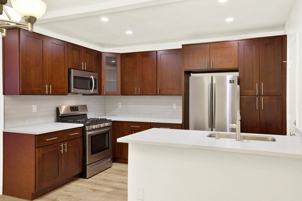 A kitchen with brown cabinets and a white counter at Wooster Encore Apartments, Los Angeles, CA 90035