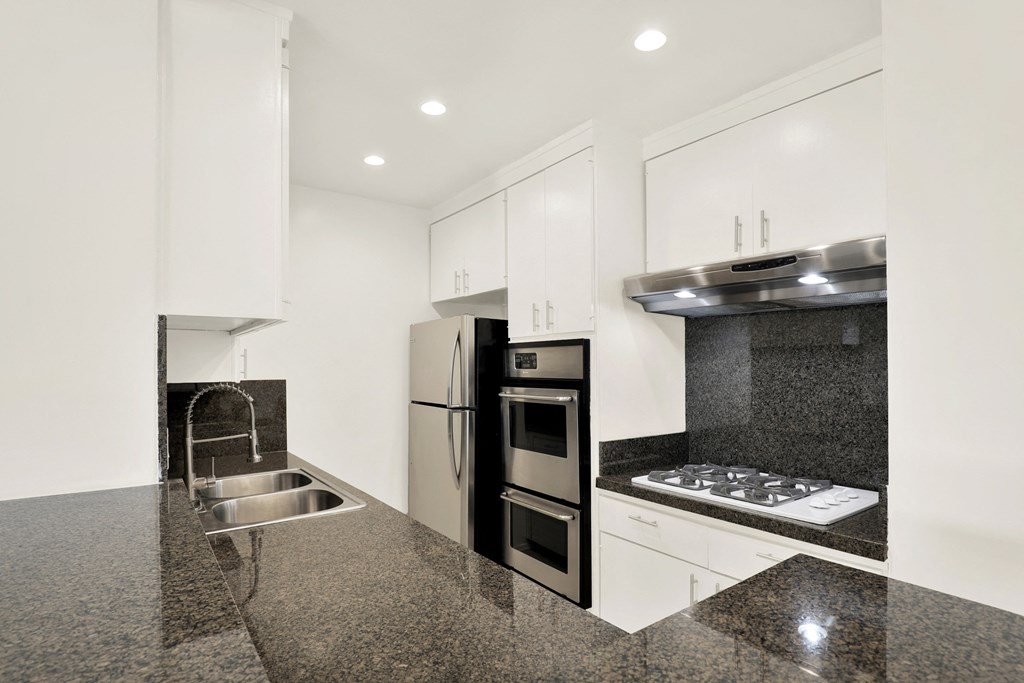 A modern kitchen with granite countertops and stainless steel appliances at Wooster Encore Apartments, Los Angeles