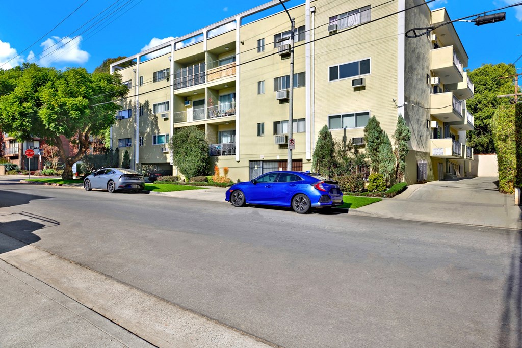 A blue car is parked on the side of a street in front of a building at Wooster Encore Apartments, California
