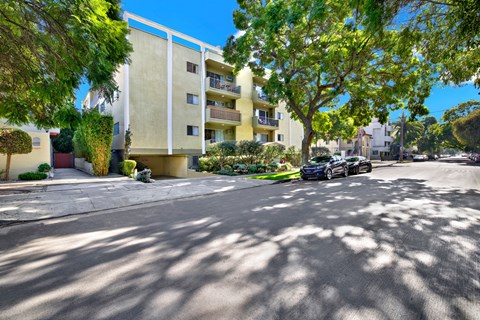 A car is parked on the street in front of a yellow building at Wooster Encore Apartments, Los Angeles, CA