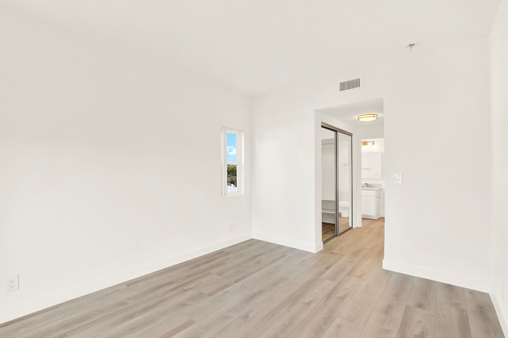 A room with a wooden floor and a white wall with a window.