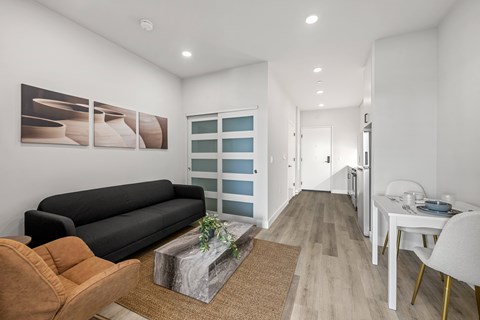 A modern living room with a black sofa, a wooden coffee table, and a dining area with a white table and chairs.