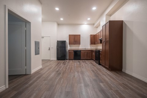 an empty kitchen with wooden floors and cabinets and a black refrigerator