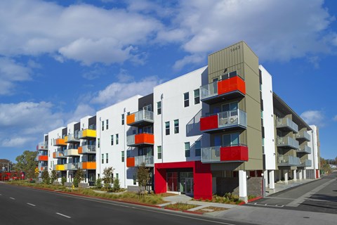 A modern multi-story apartment building with balconies and a mix of red, yellow, and white colors.