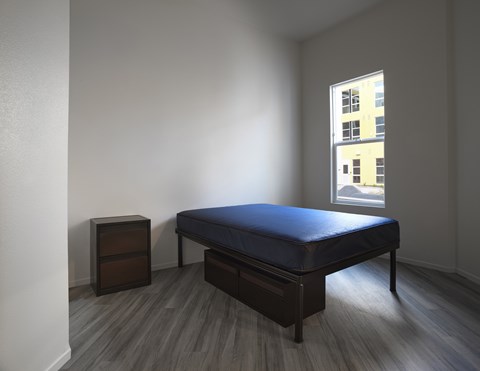 A bedroom with a bed, nightstand and window.
