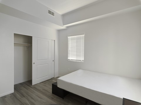 A white bedroom with a bed, dresser, and window.