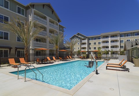 A swimming pool surrounded by orange lounge chairs and palm trees.