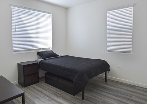 A bedroom with a bed, nightstand, and window with blinds.