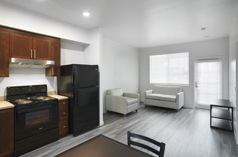 A black refrigerator sits in a kitchen with wooden cabinets and a stove.