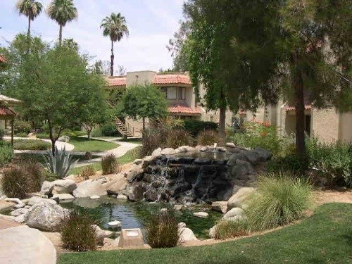 A garden with a waterfall and a house in the background.