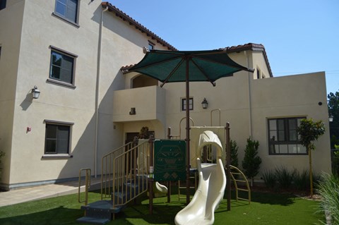 a playground with a slide and an umbrella in front of a building
