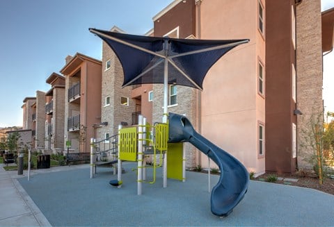 a playground with a blue slide and an umbrella