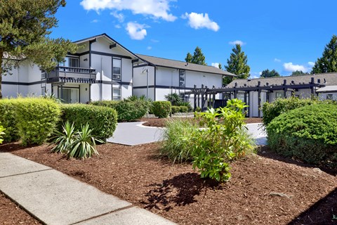 A white building with a black roof and a green bush in front.