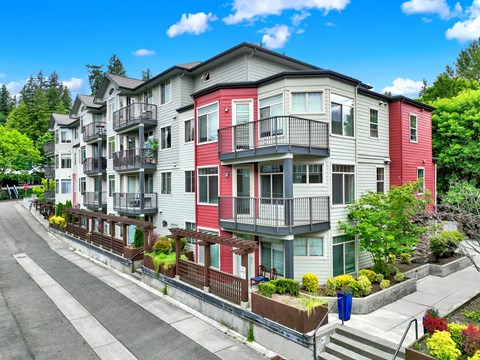 A row of multi-story apartment buildings with balconies and flower pots on the steps.