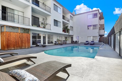 A pool surrounded by a patio with a bench and a building in the background.