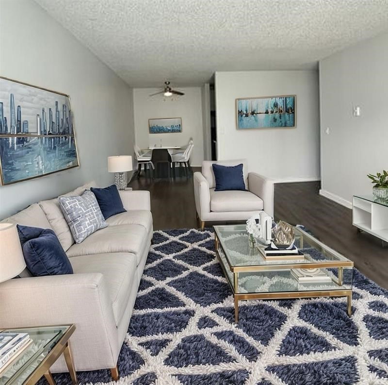 A living room with a white couch, a glass coffee table, and a blue rug.