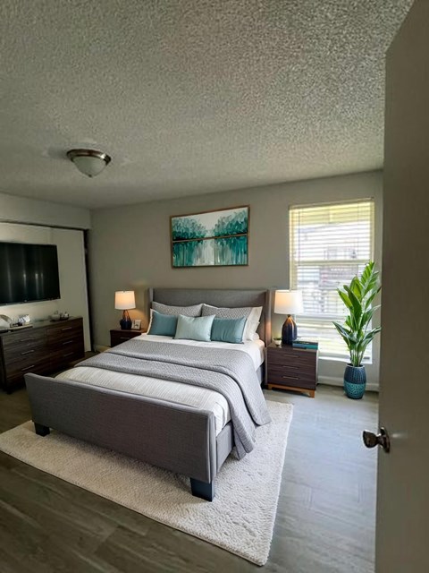 A bedroom with a large bed, a nightstand with a lamp, and a painting on the wall.