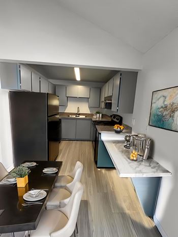 A modern kitchen with a black countertop and white chairs.