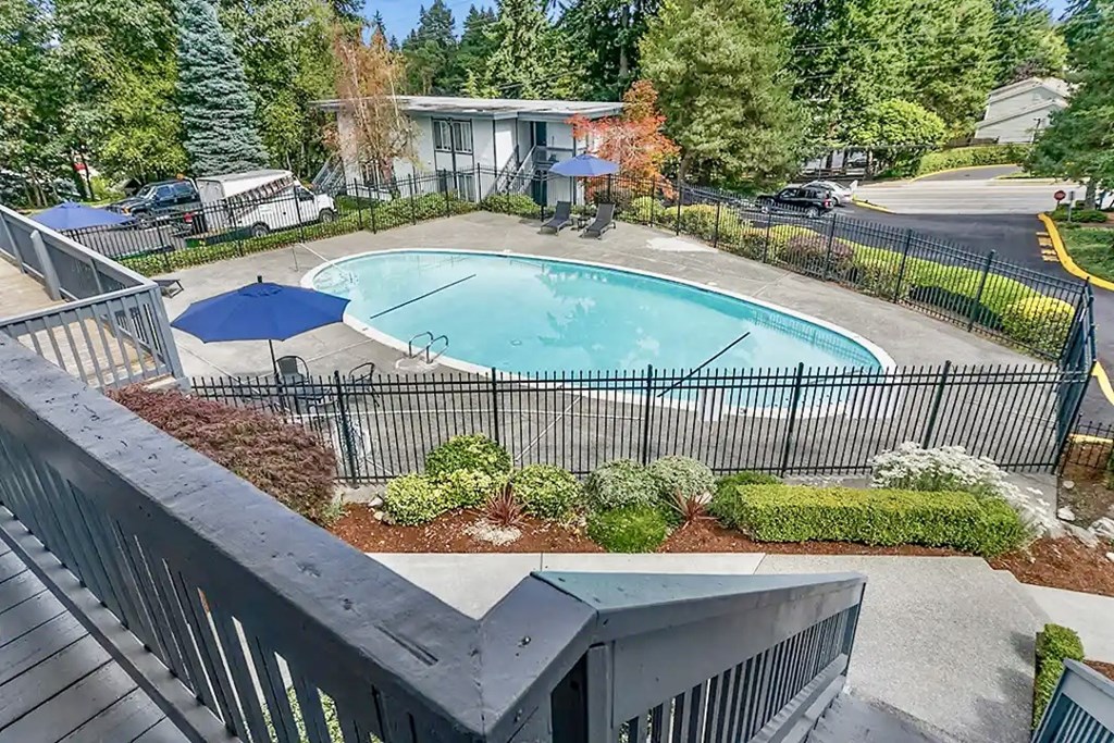 Swimming pool surrounded by a black fence and a blue umbrella at Capri Apartments, Mountlake Terrace, WA, 98043