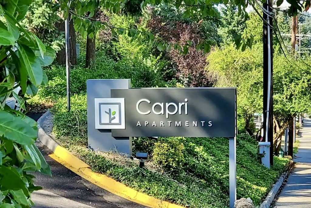 Sign for Capri Apartments is shown in front of a green landscape at Capri Apartments, Mountlake Terrace, 98043