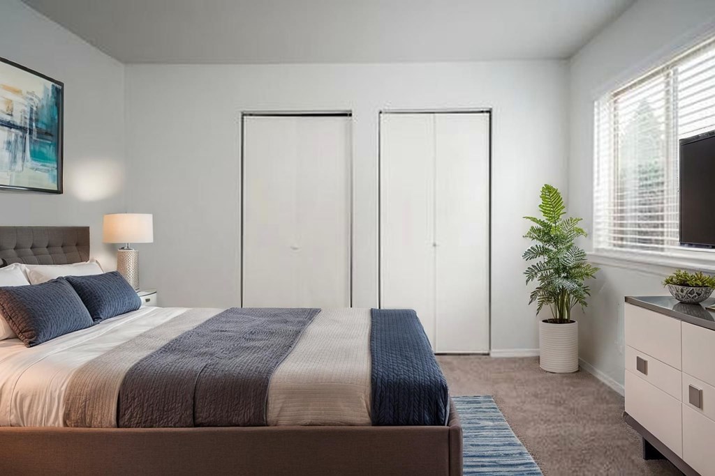 A bedroom with a bed, two doors, a nightstand, and a plant.