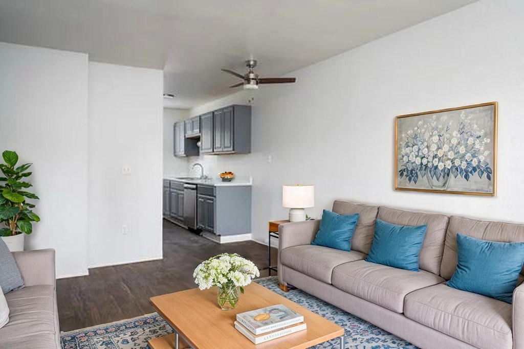 A living room with a grey couch, a wooden table, a ceiling fan, and a painting on the wall.