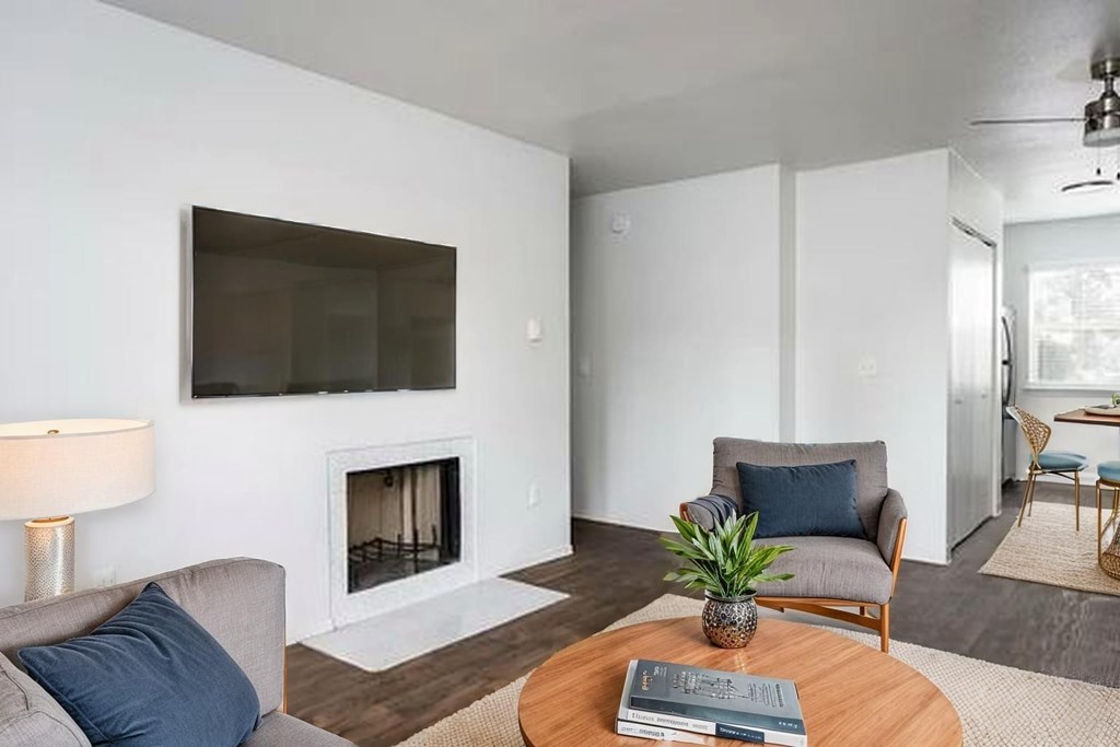 A living room with a grey couch, a wooden table, a potted plant, and a television mounted on the wall.