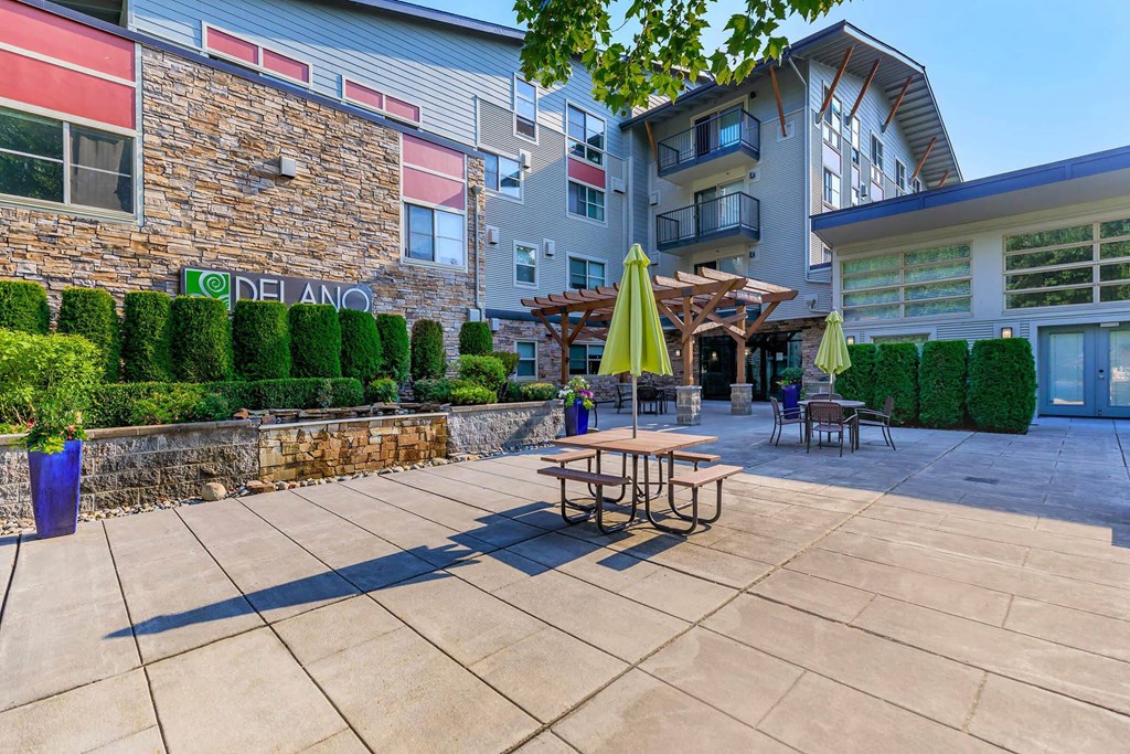 a patio with tables and umbrellas outside of an apartment building at Delano, Redmond, WA 98052
